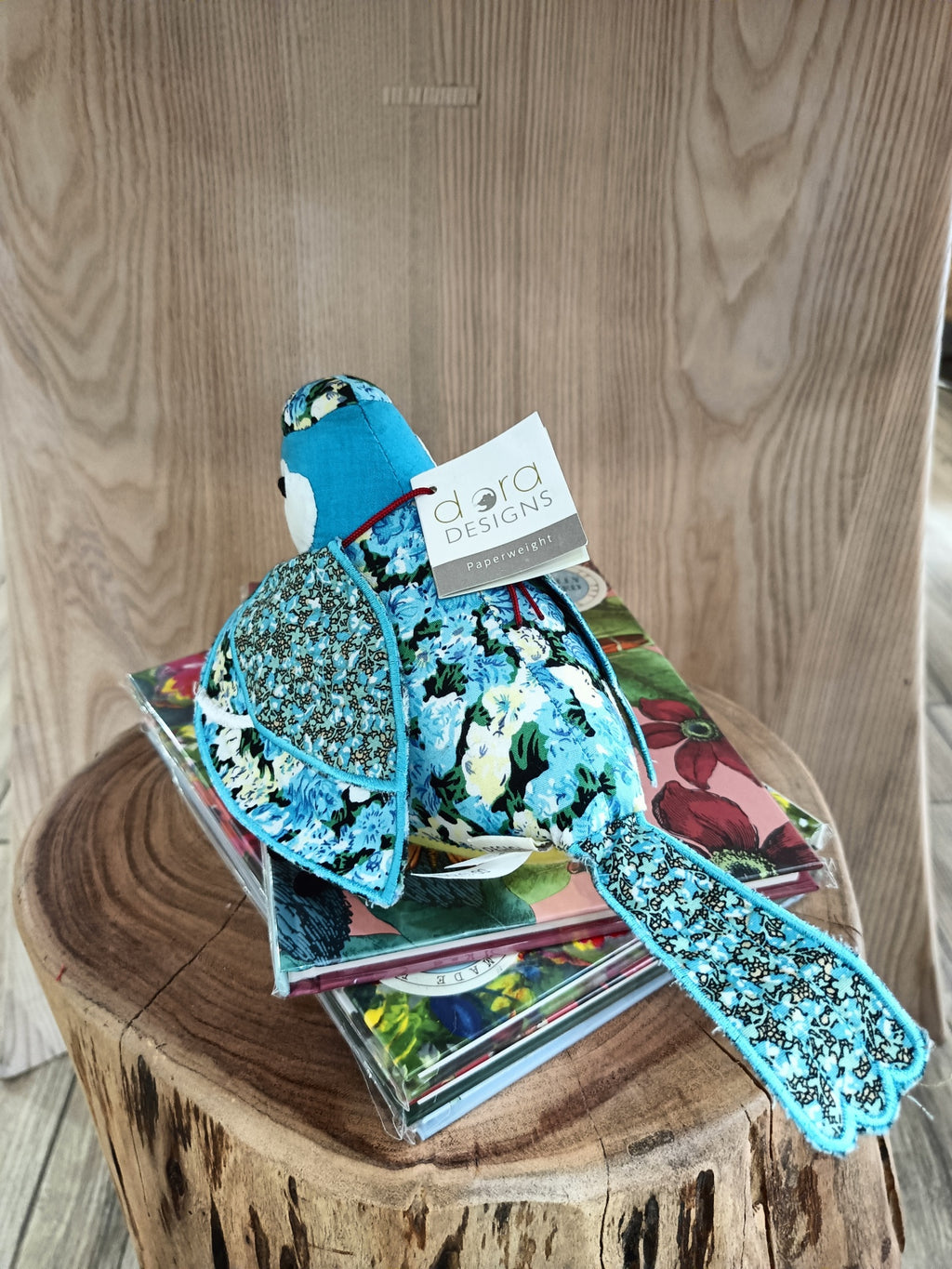 Pássaro de tecido azul com padrão floral, livros coloridos, tronco de madeira