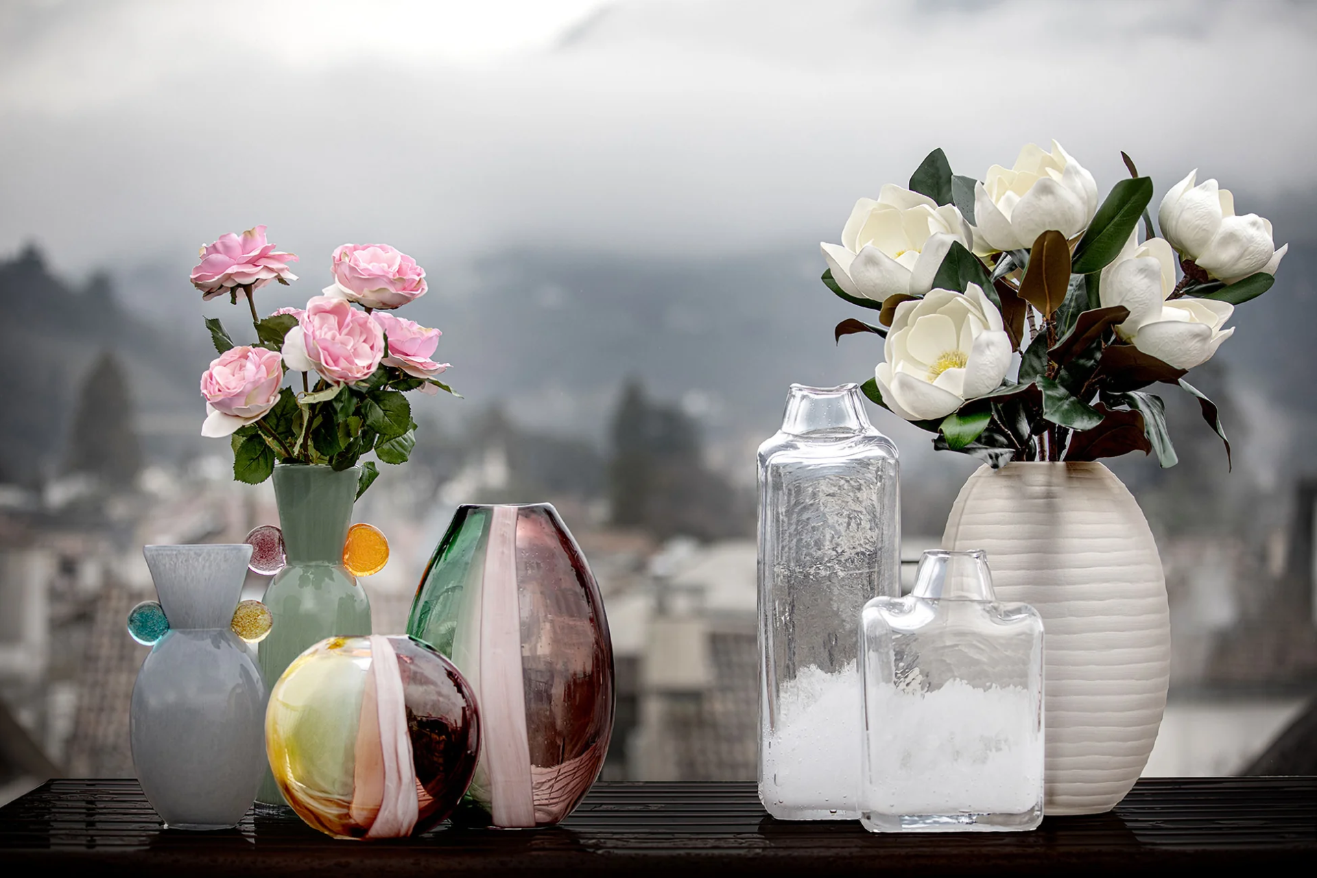 Vasos de vidro com flores artificiais rosas e brancas sobre superfície escura