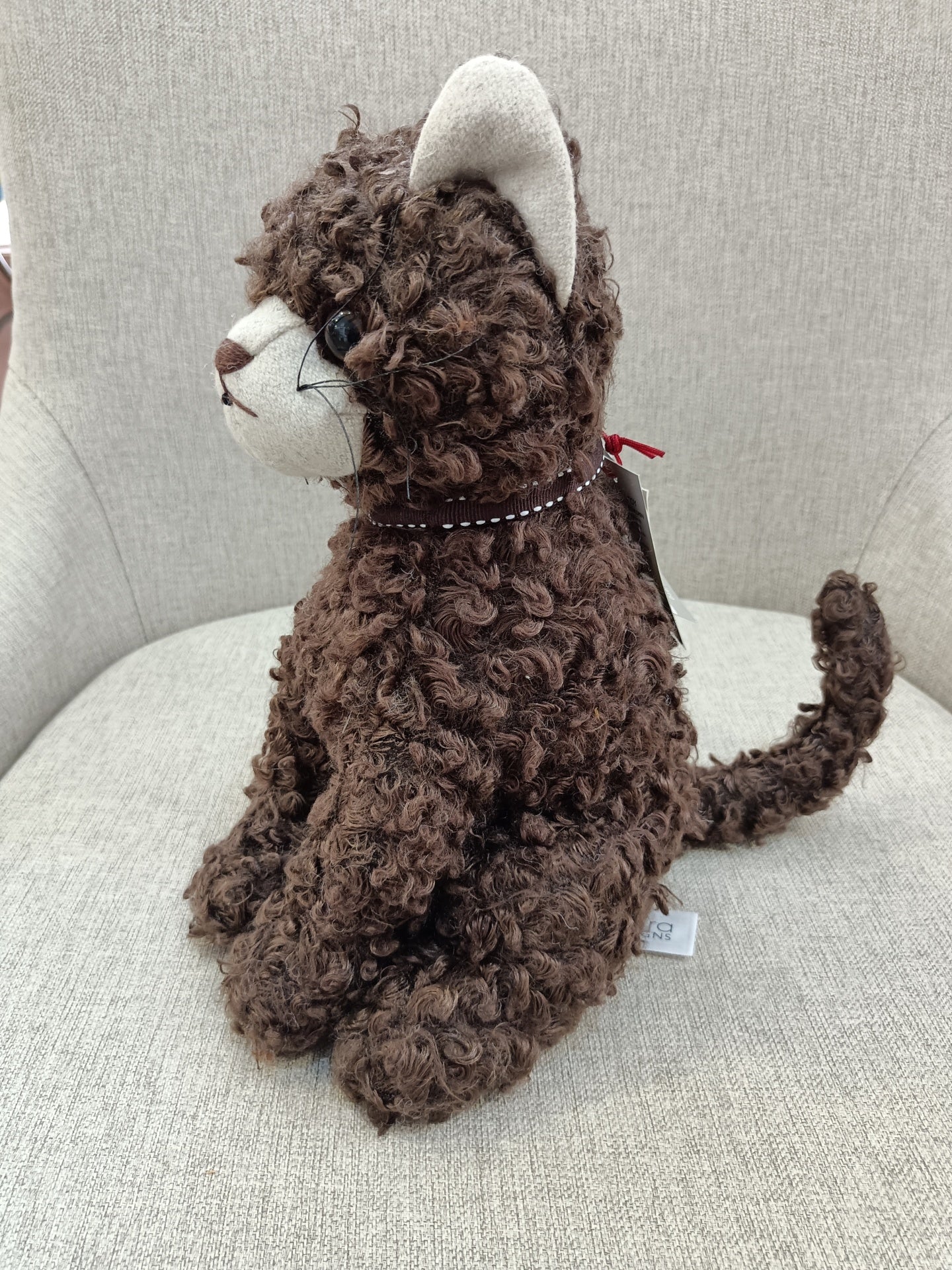 Boneco de peluche com aspeto de gato castanho num cadeirão cinza