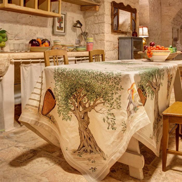 Toalha de mesa com padrão de oliveiras e cestos sobre mesa de madeira numa cozinha rústica