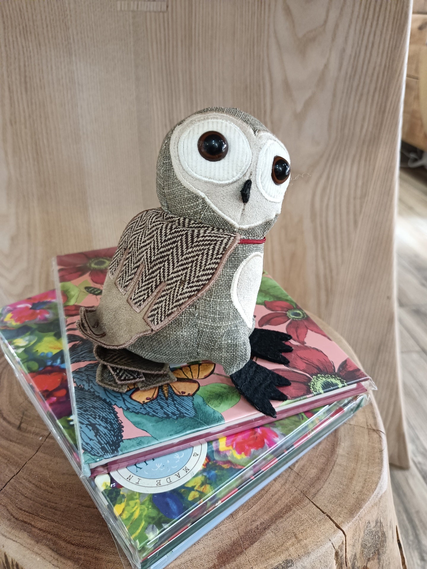 Boneco coruja tecido em cima de caixas com capas florais sobre mesa de madeira