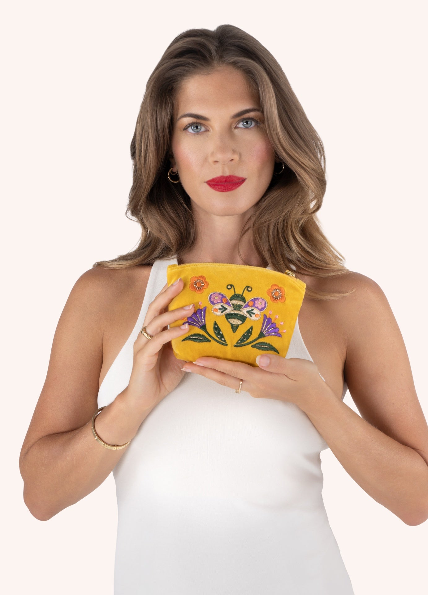 Carteira amarela bordada com flores e inseto segura por mulher com vestido branco