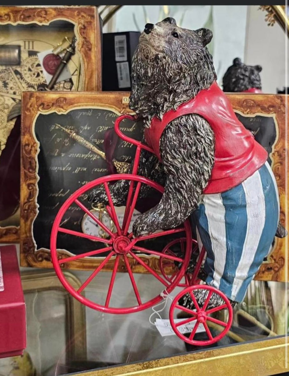 Estatueta de urso a andar de bicicleta com colete vermelho e calções riscas azuis e brancos