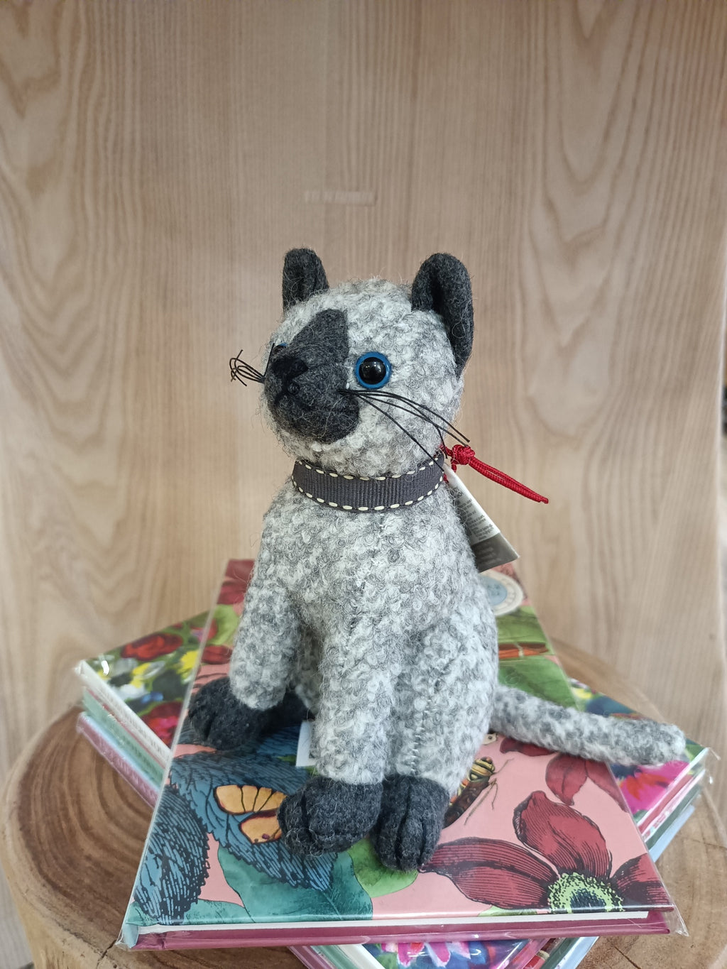 Boneco de gato de feltro cinzento e preto sobre notebooks com capas florais