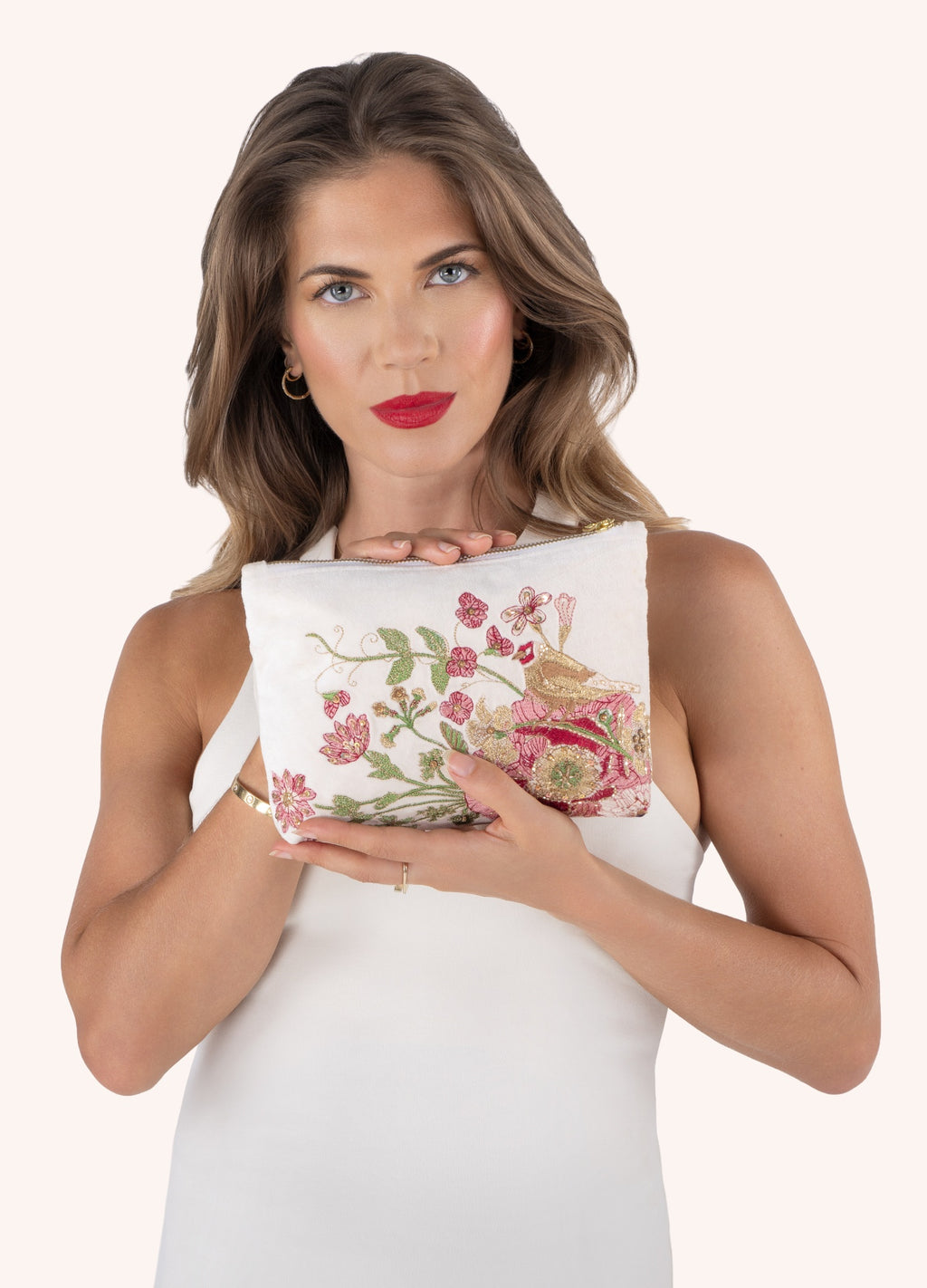 Mala de mão branca bordada com flores e pássaro, mulher a segurá-la com vestido branco.