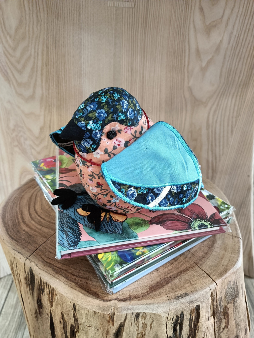 Boneco de pato de tecido estampado sobre livros coloridos em tronco de madeira