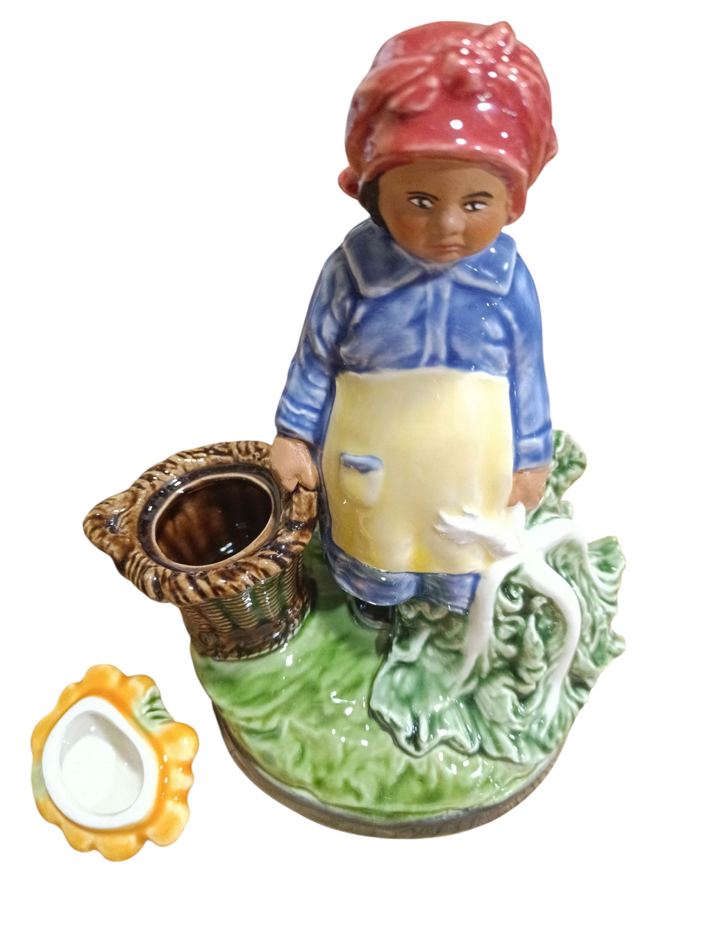 Figura decorativa em porcelana de mulher vestida em azul e amarelo com lenço vermelho, segurando uma cesta, sobre base verde com tigela amarela ao lado