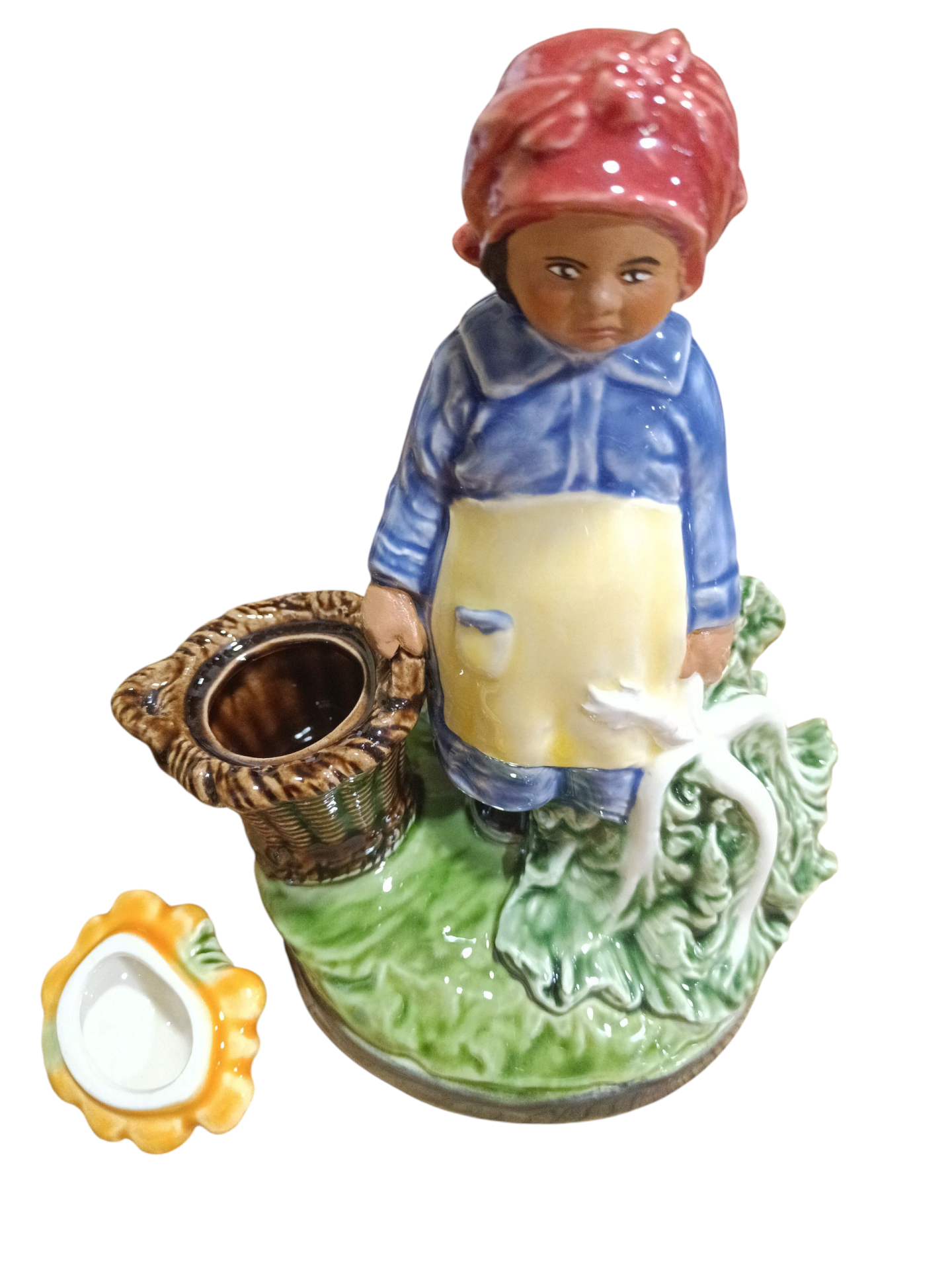 Figura decorativa em porcelana de mulher vestida em azul e amarelo com lenço vermelho, segurando uma cesta, sobre base verde com tigela amarela ao lado