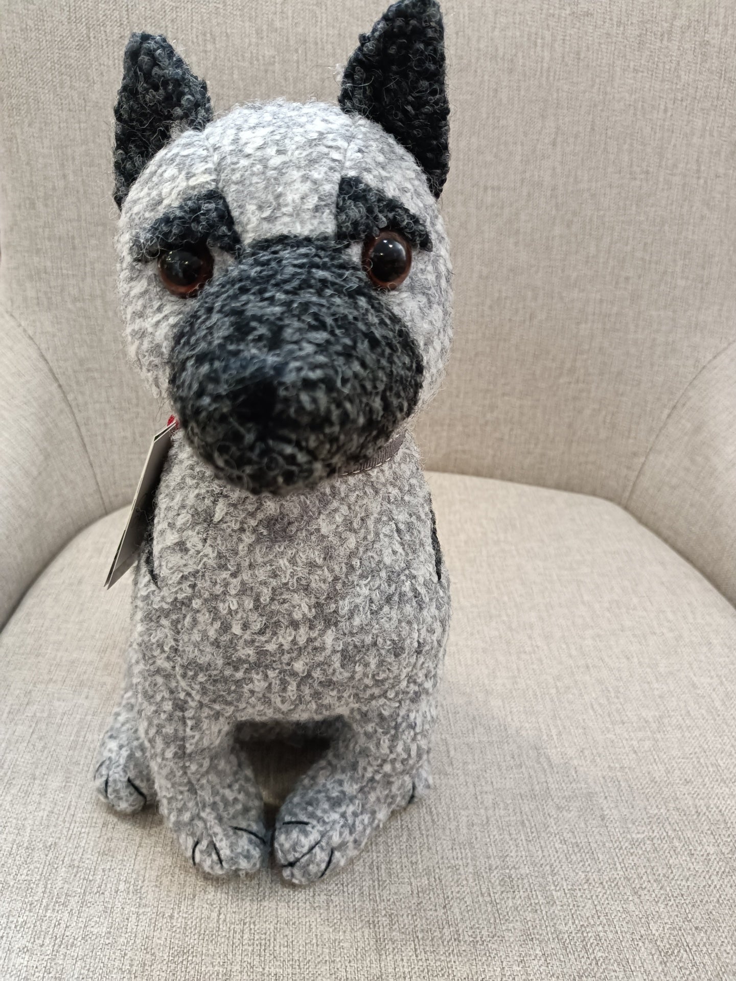 Boneco de pelúcia cinza de cão sentado sobre tecido cinza claro