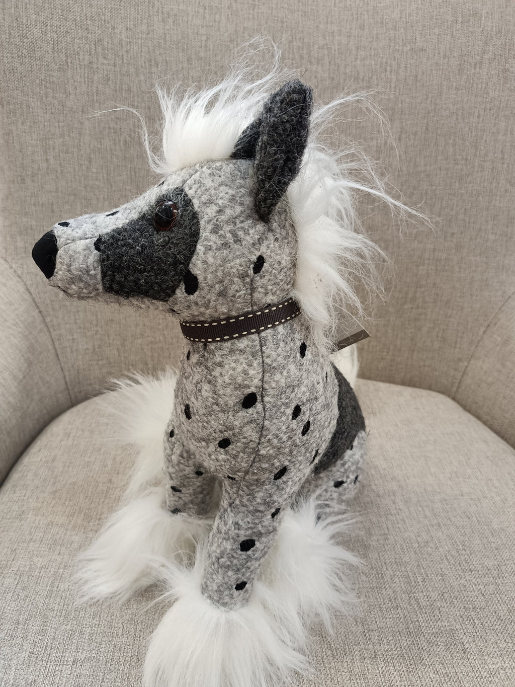Pelúcia de cão cinzento com manchas pretas e pelo branco sentado numa cadeira cinzenta.