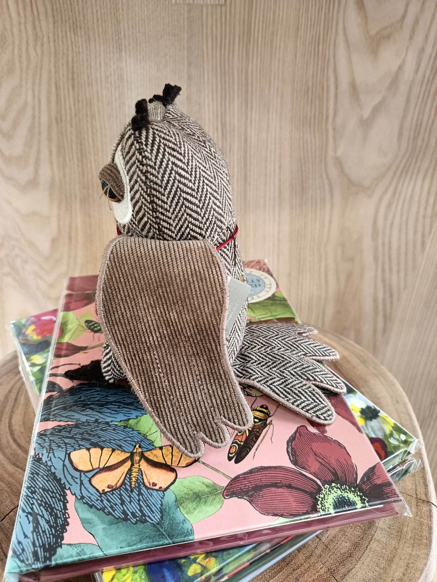 Pelúcia de coruja em tecido com padrão espinha de peixe e veludo cotelê, sobre cadernos florais e borboletas, em madeira clara