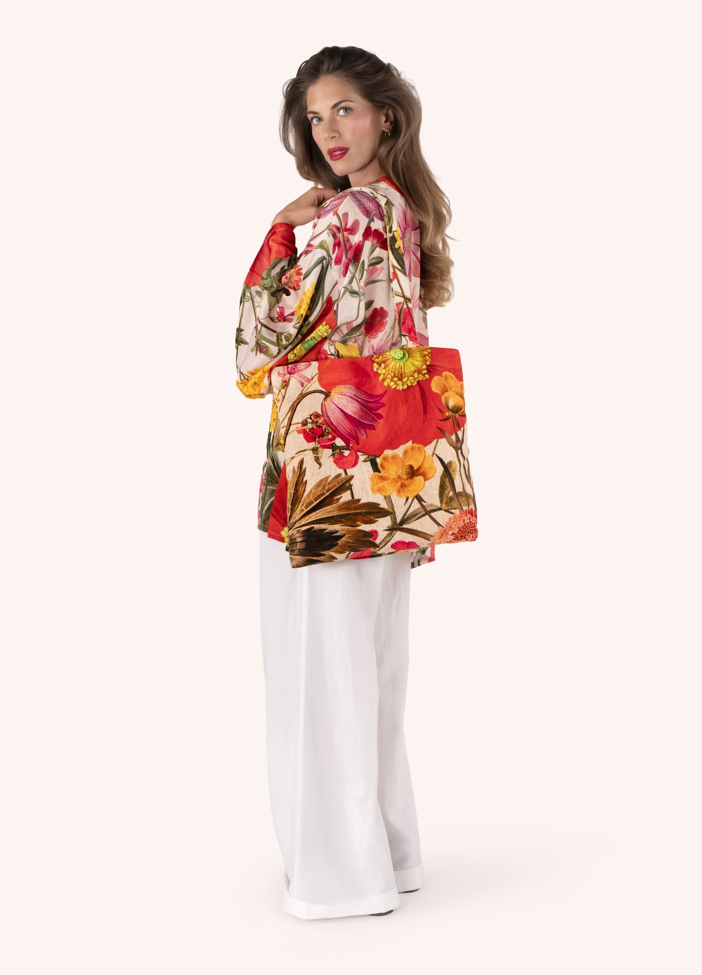 Mulher de blusa estampada e calças brancas a usar uma cadeira de tecido floral colorida