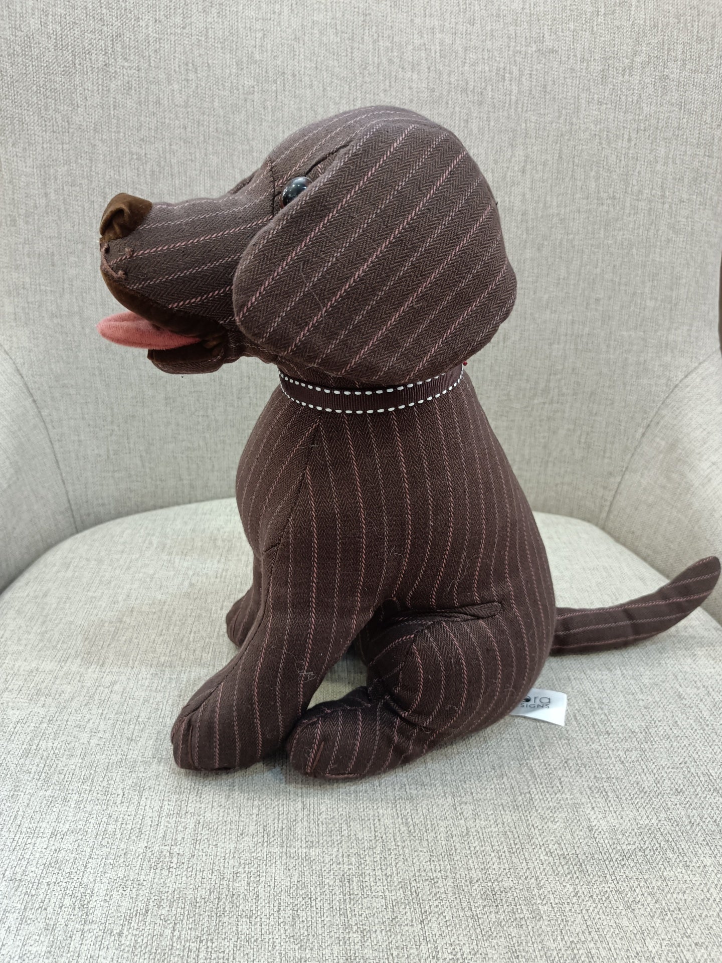 Pelúcia de cão castanho riscado sentado numa cadeira cinza