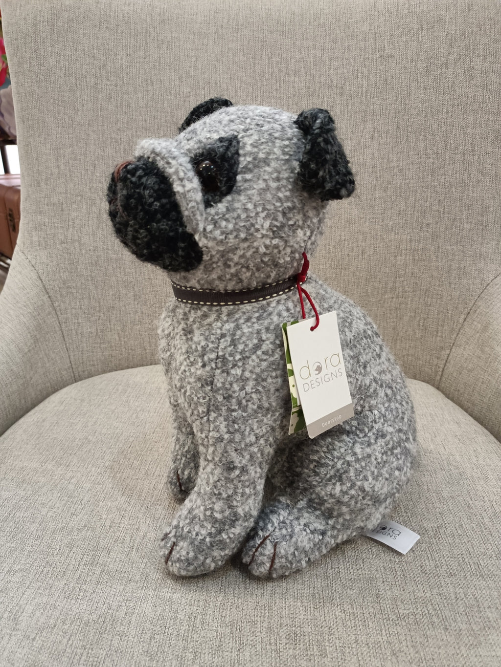 Boneco de cachorro cinzento e preto com coleira castanha e etiqueta sentado numa cadeira cinzenta