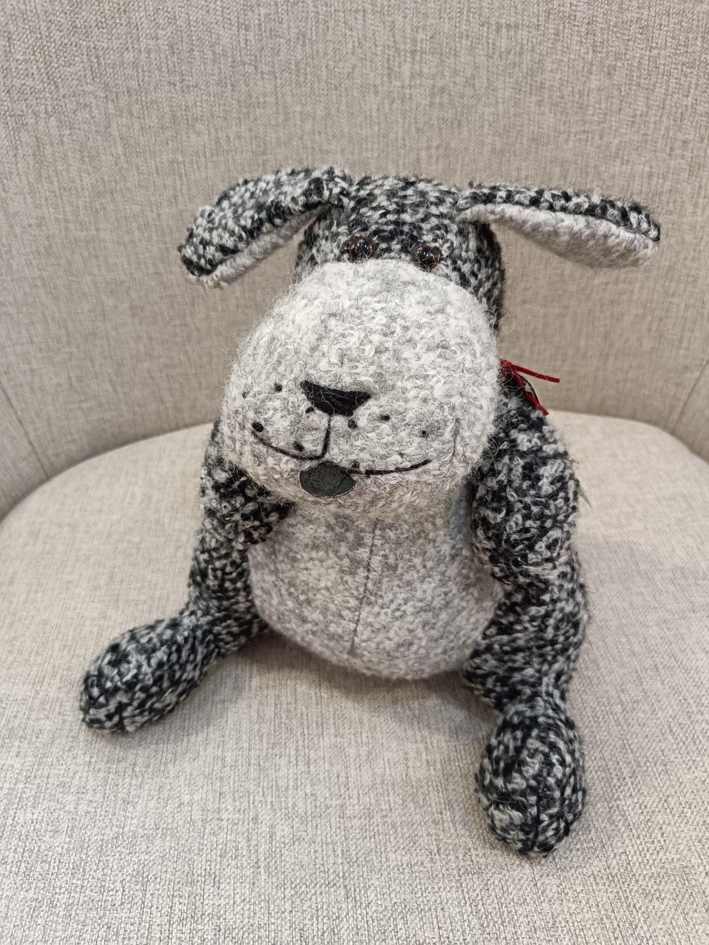 Boneco de cão em tecido cinza sentado num sofá cinzento claro