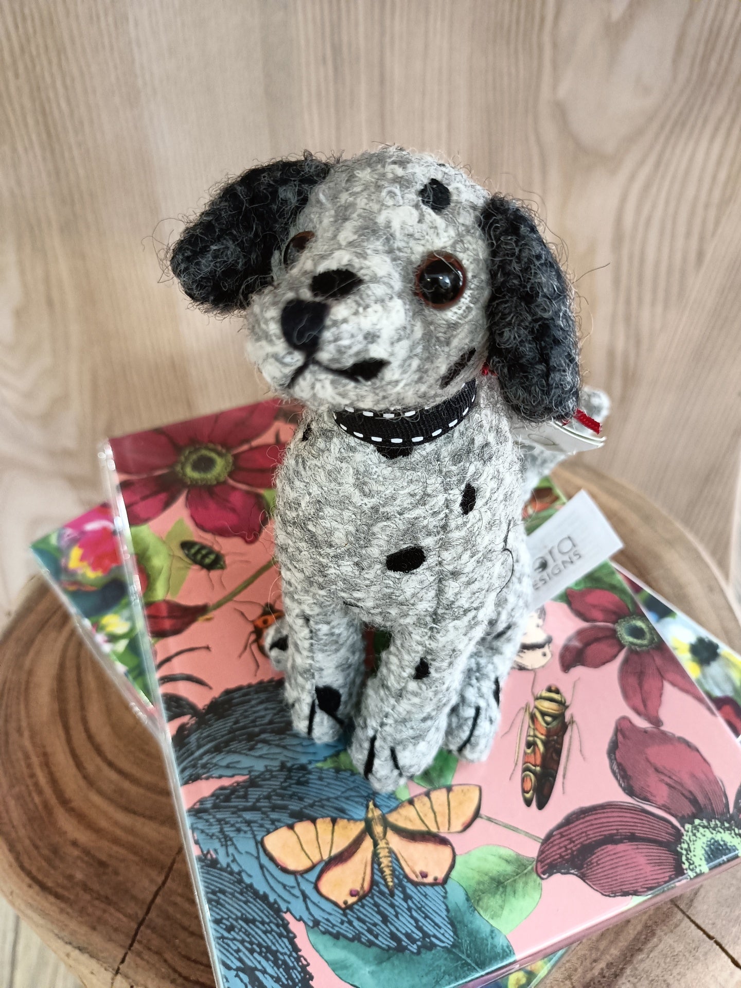 Pelúcia de cão cinzento com manchas pretas sentada sobre capas coloridas com flores e borboletas