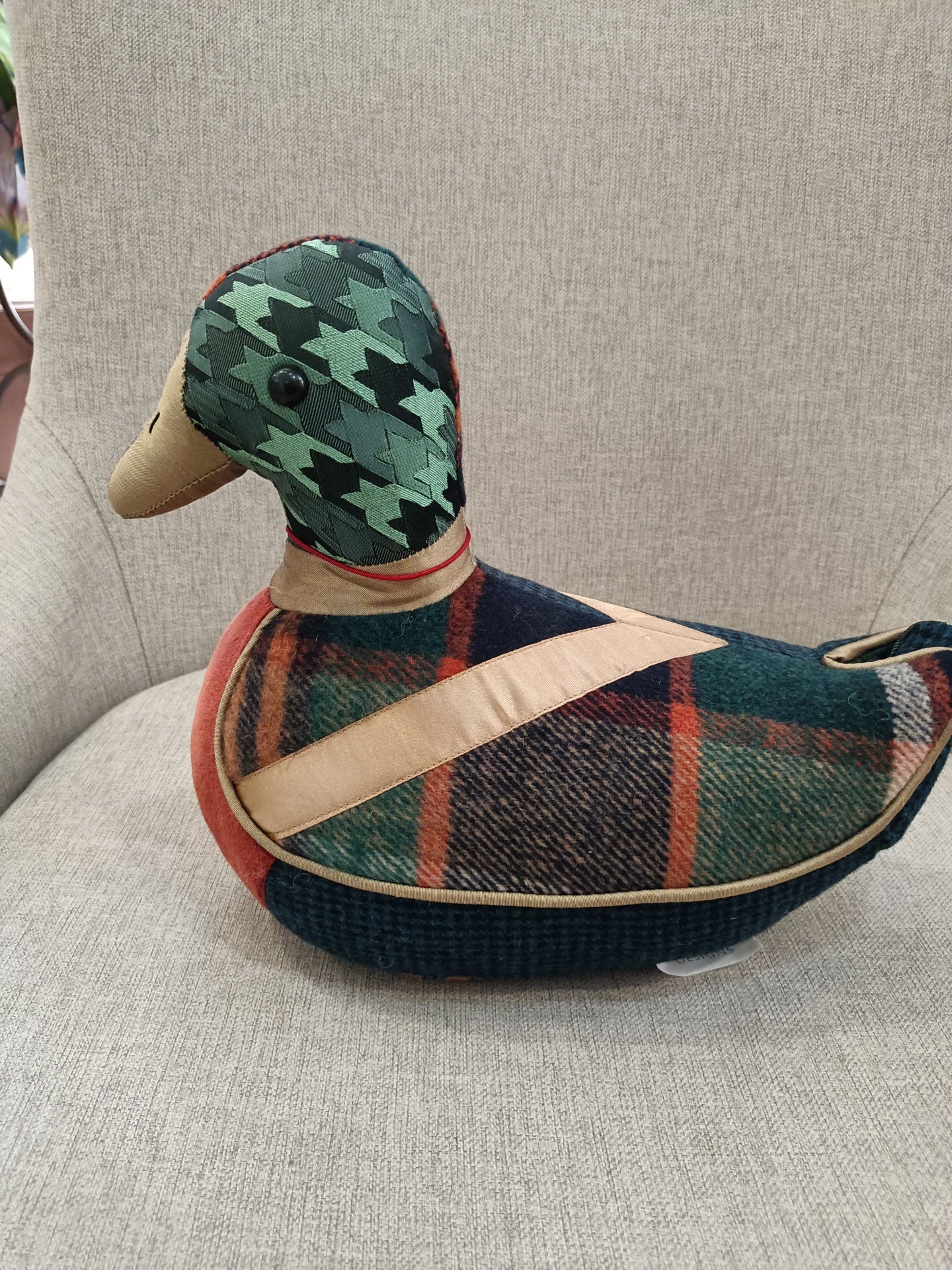 Boneco decorativo em forma de pato com padrões pied-de-poule e xadrez sentado numa cadeira cinzenta