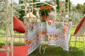 Mesa de ferro com toalha floral e almofadas vermelhas num jardim