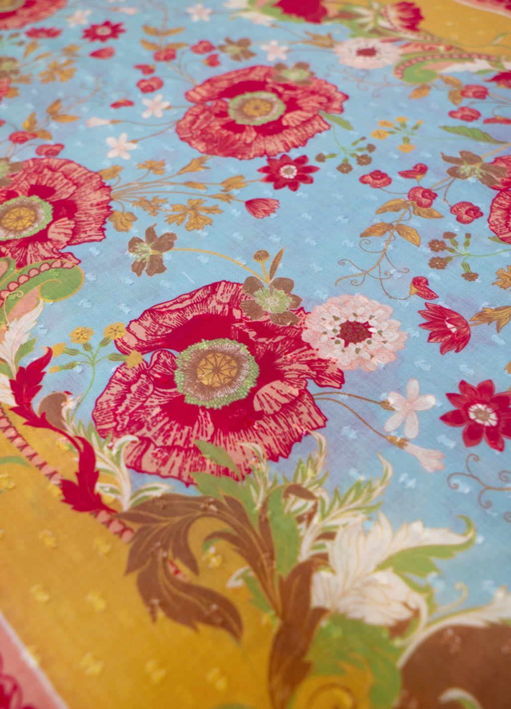 Tecido com padrão floral colorido em fundo azul e detalhes decorativos.