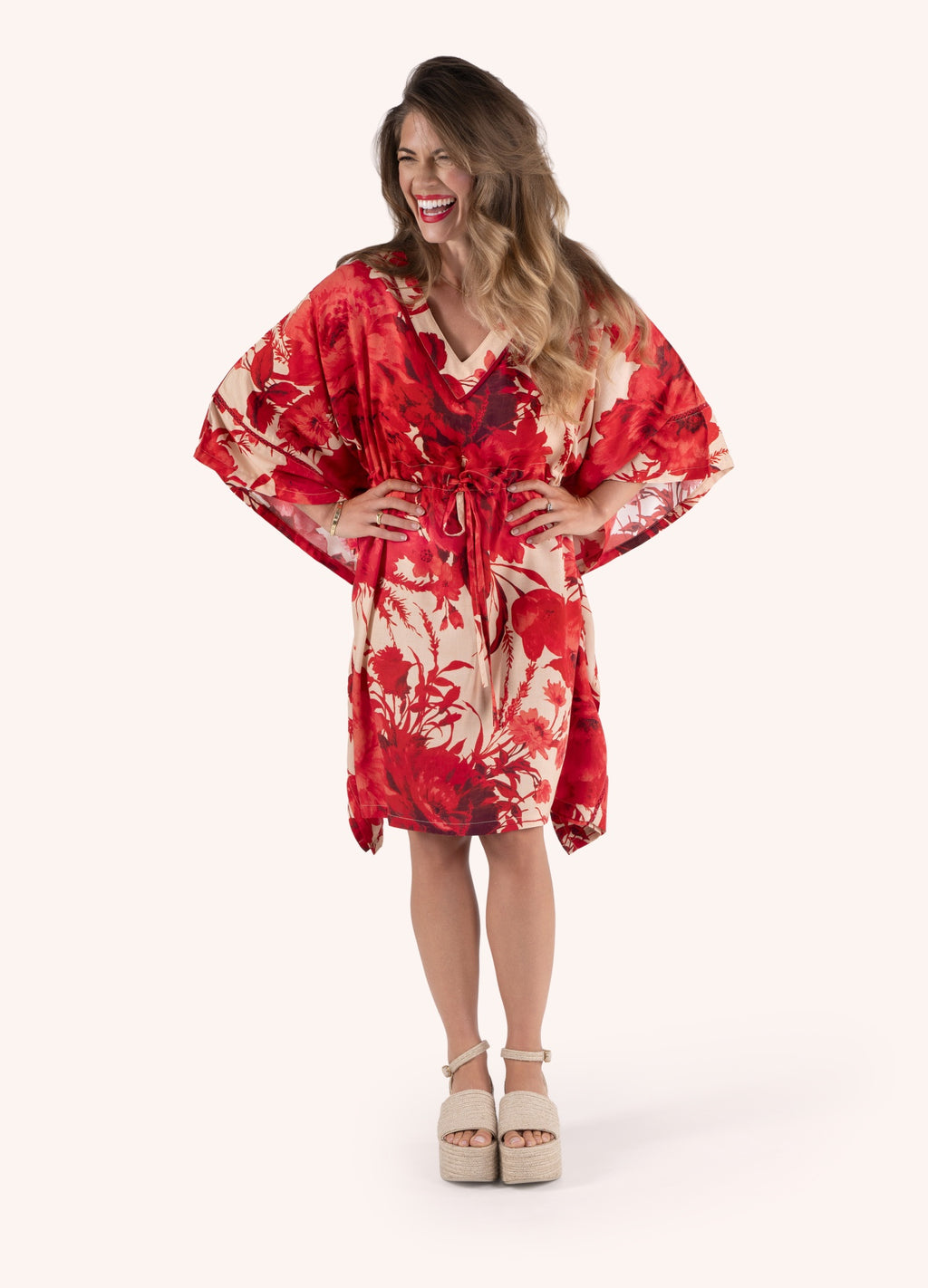 Vestido floral vermelho e bege com cintura ajustável e sapatos de salto beige.