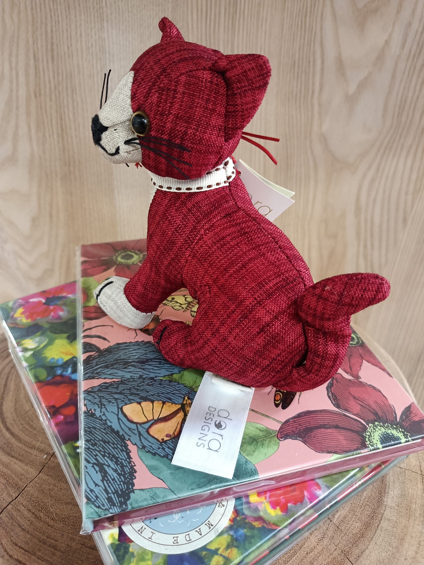 Brinquedo de gato de tecido vermelho em cima de caixas coloridas com flores.