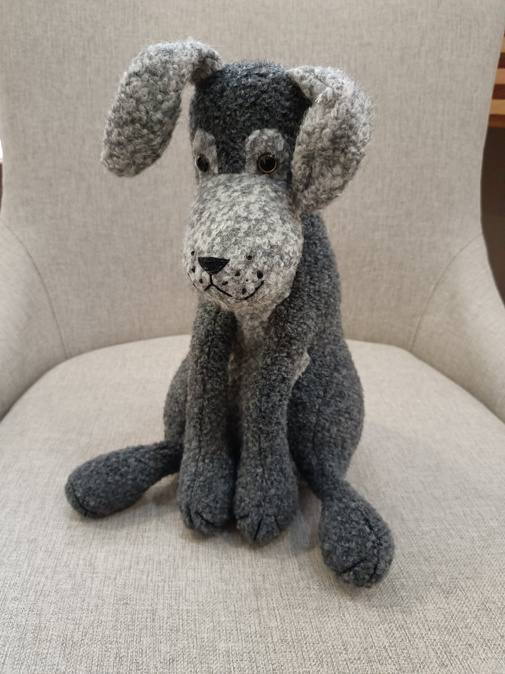 Boneco de cão cinza e preto sentado numa cadeira creme