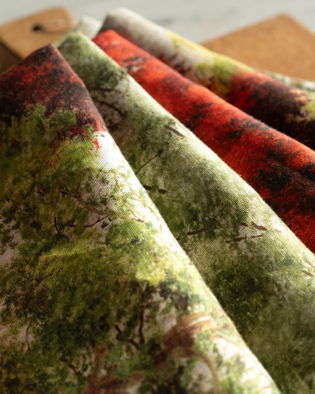 Tecido estampado com desenhos de árvores em várias cores, dobrados sobre superfície de madeira.