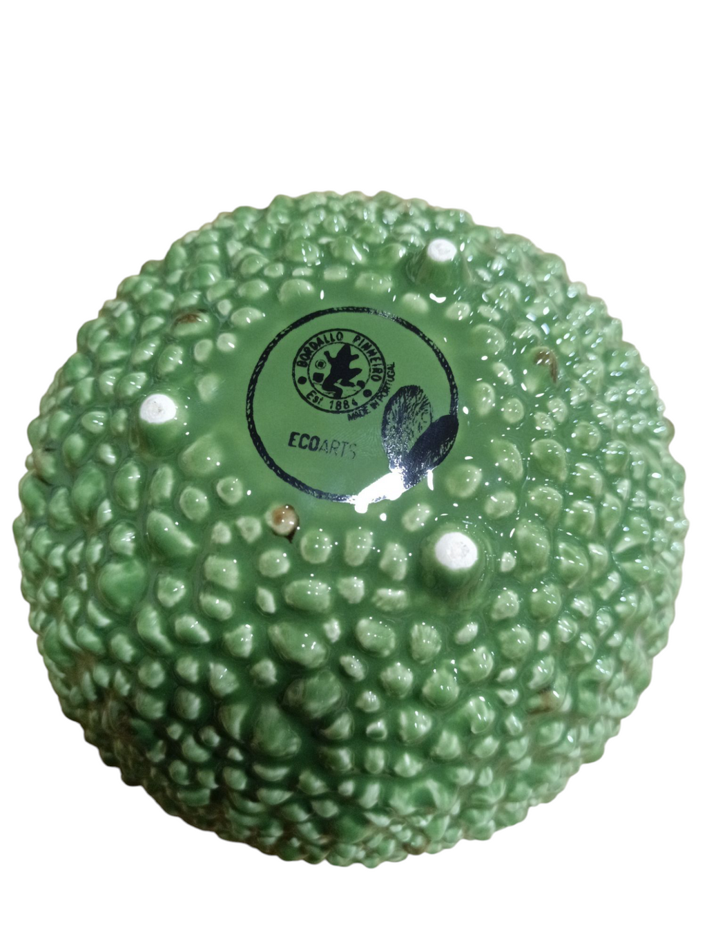 Objeto redondo verde com textura semelhante à casca de fruta e selo preto no centro