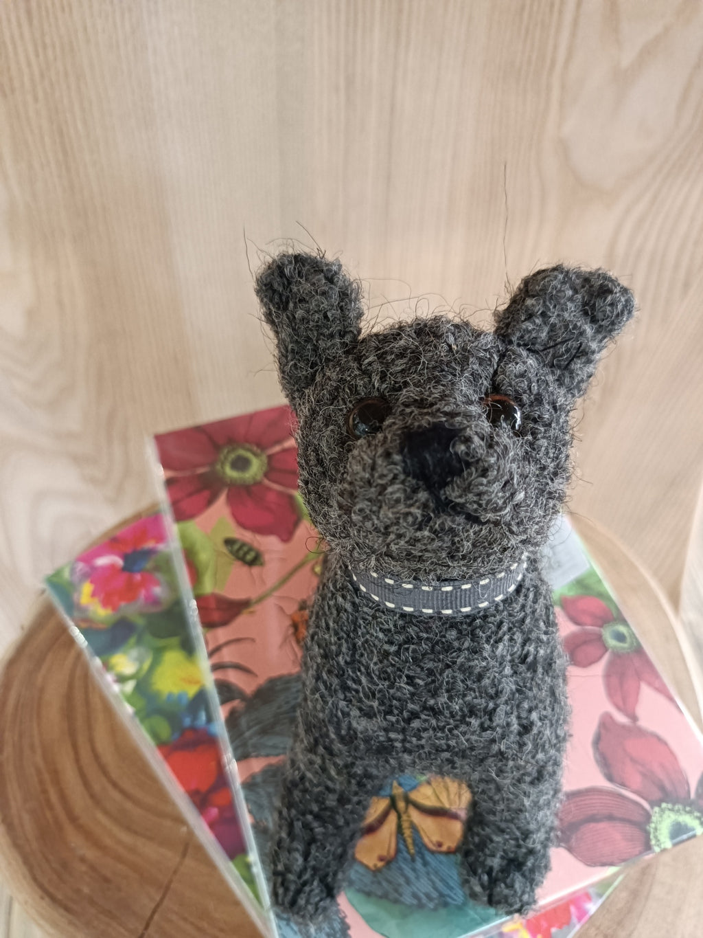 Estatueta de cão cinzento em tecido tufado sobre caixas florais coloridas e fundo de madeira