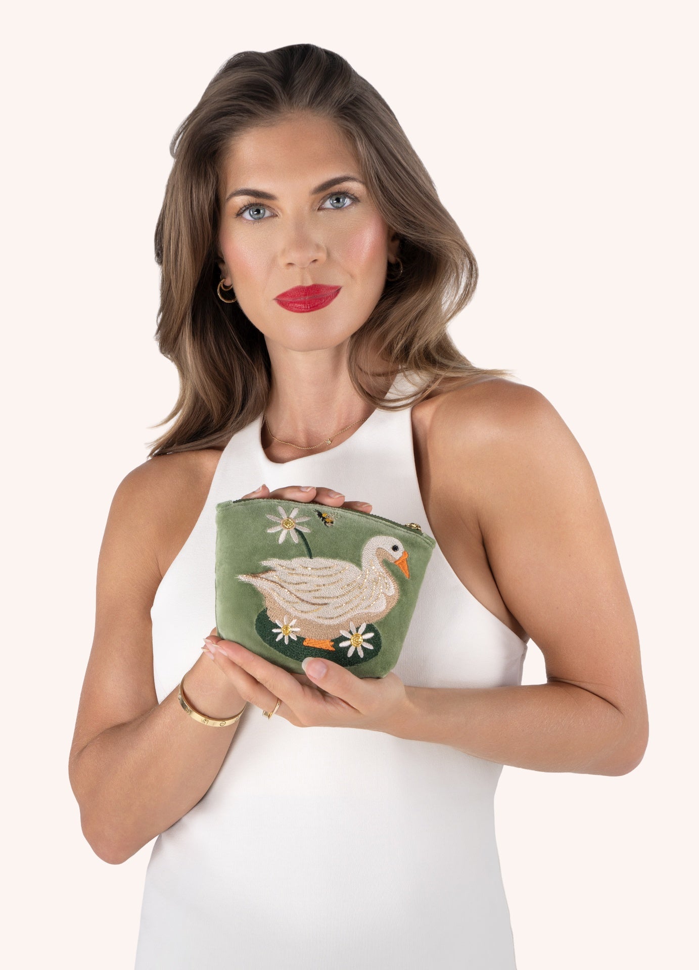 Carteira verde bordada com cisne, flores e abelha segurada por mulher com vestido branco