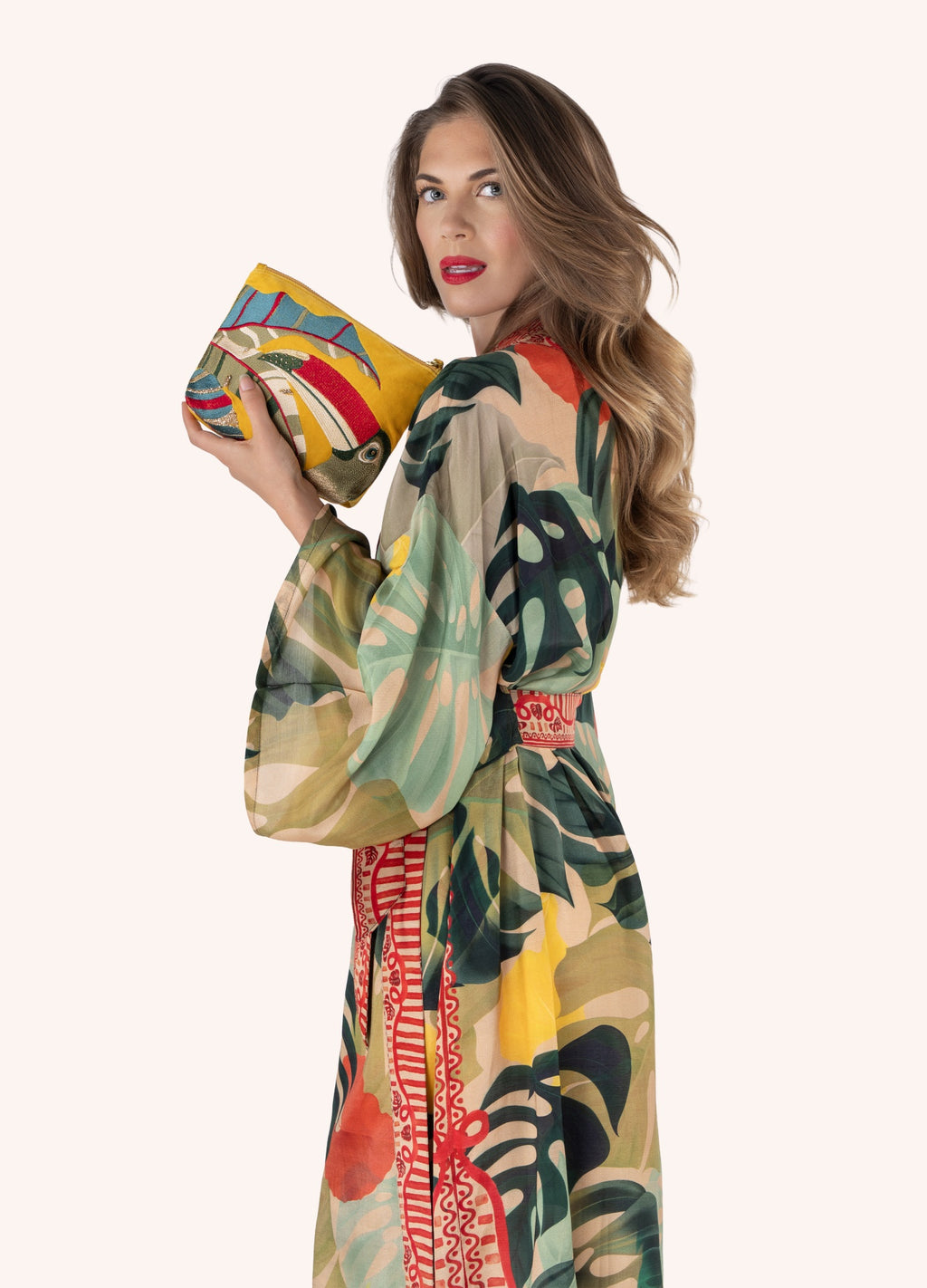 Mulher com vestido estampado tropical segurando bolsa amarela bordada.