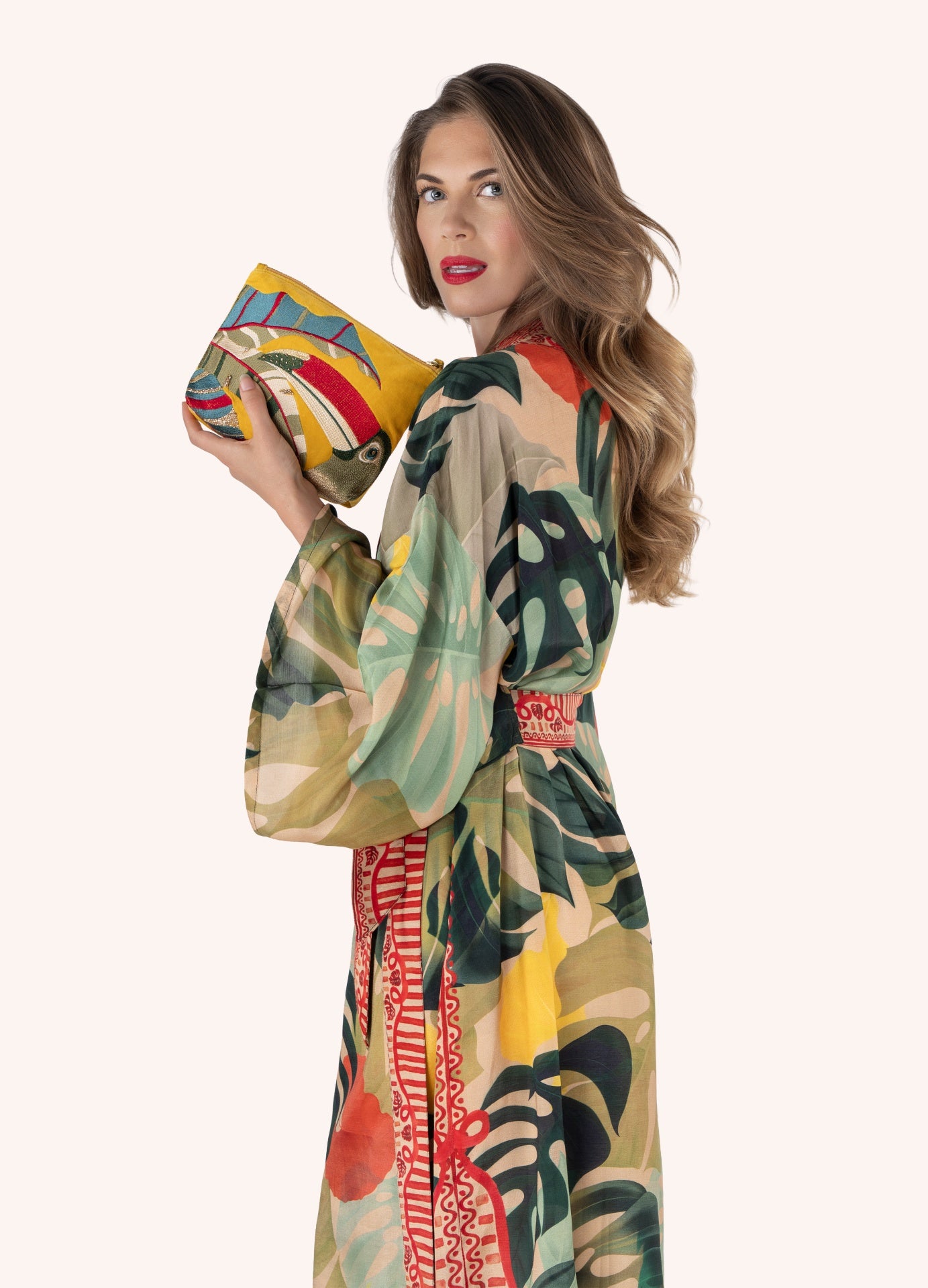 Mulher com vestido estampado tropical segurando bolsa amarela bordada.