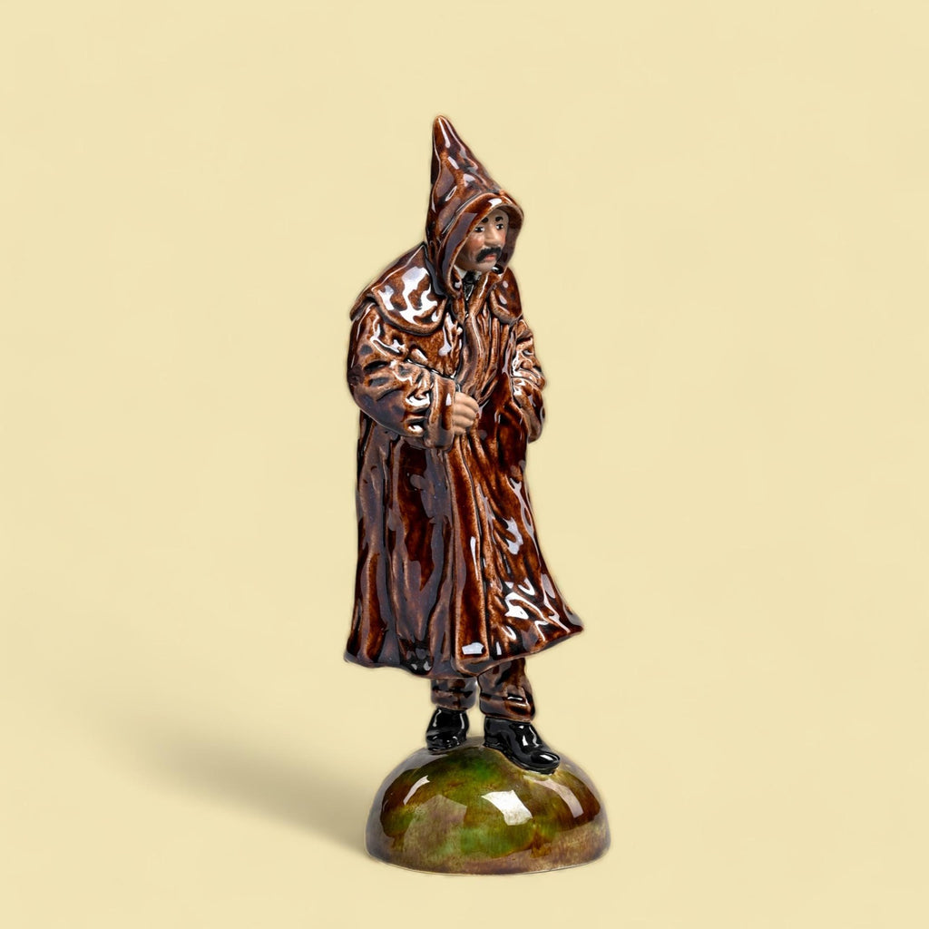 Figura cerâmica de homem com capa e capuz castanhos em base verde e castanha