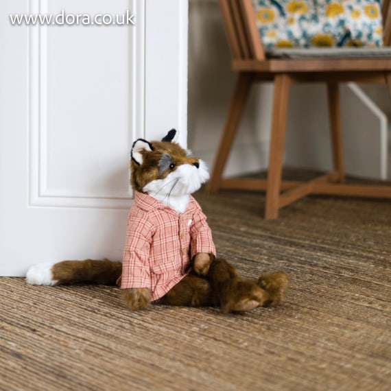Urso de peluche castanho com camisa rosa sentado no chão junto a uma porta branca