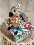 Pelúcia em forma de pássaro com tecidos estampados sobre DVDs empilhados num suporte de madeira