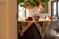 Toalha de mesa com padrão verde e vermelho sobre bancada de cozinha cinzenta com elementos decorativos.