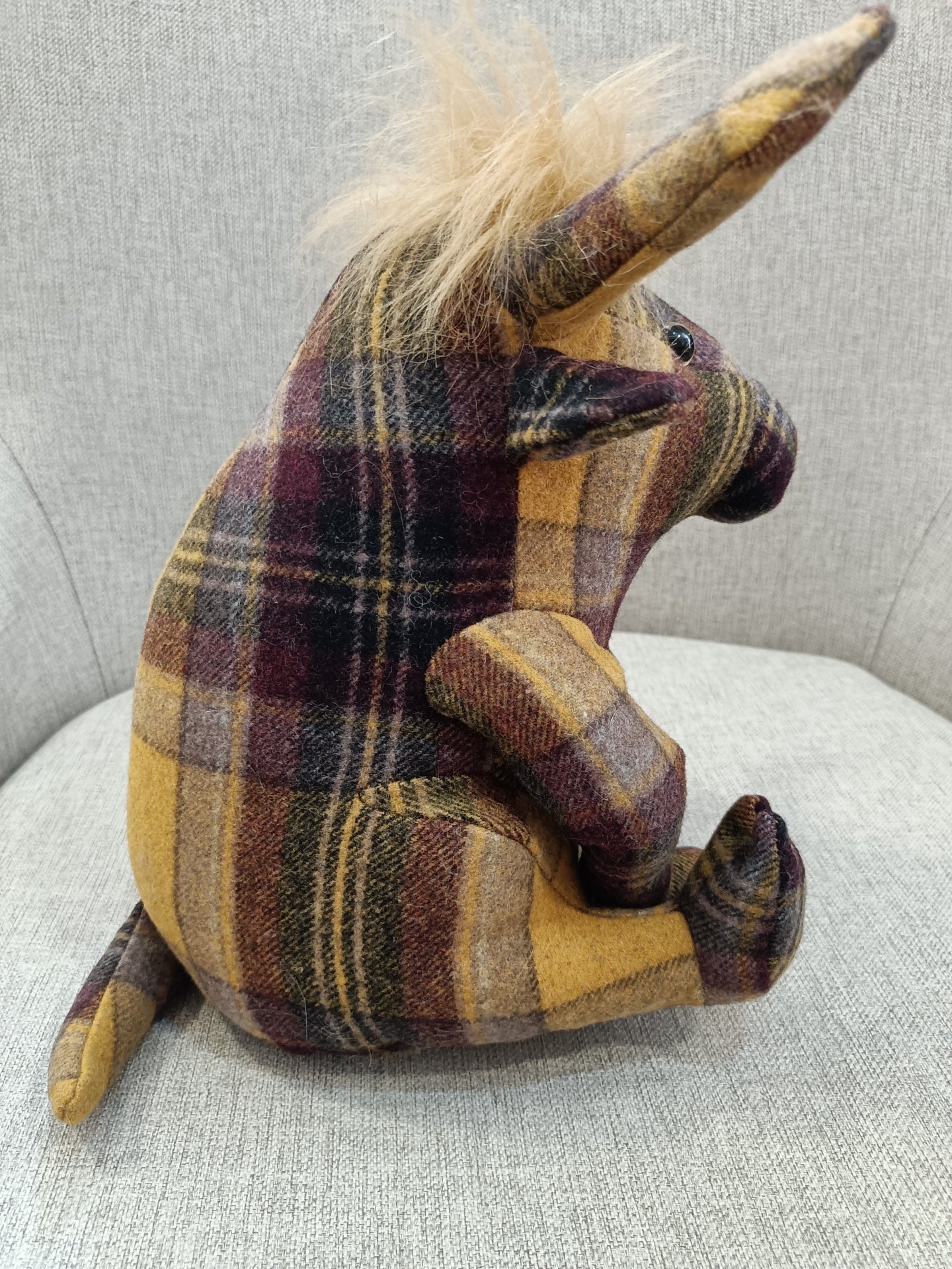 Pelúcia de unicórnio xadrez castanho e amarelo sentada em sofá cinza