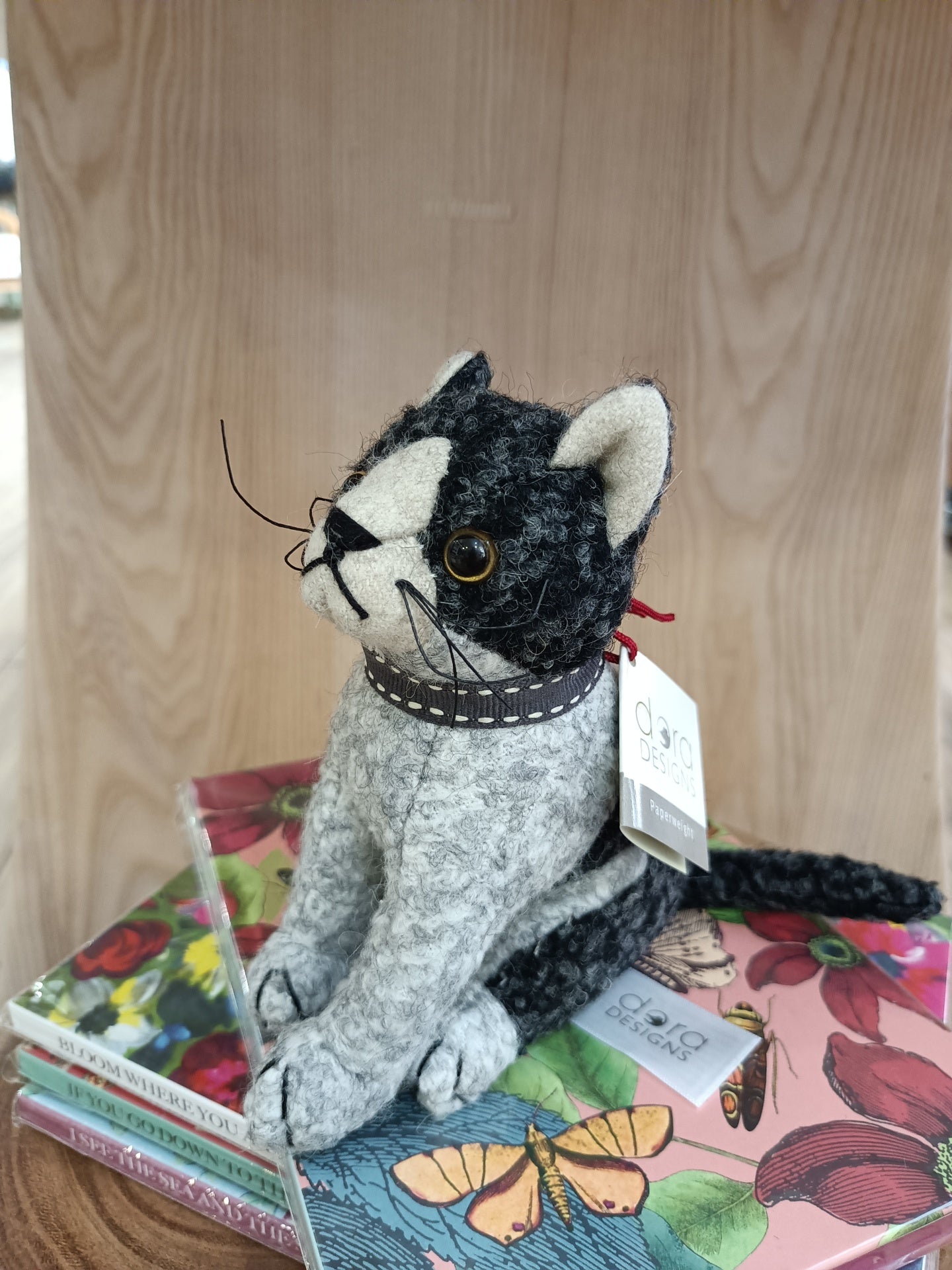 Boneco decorativo de gato em tecido cinzento e preto sobre livros coloridos com capa ilustrada.