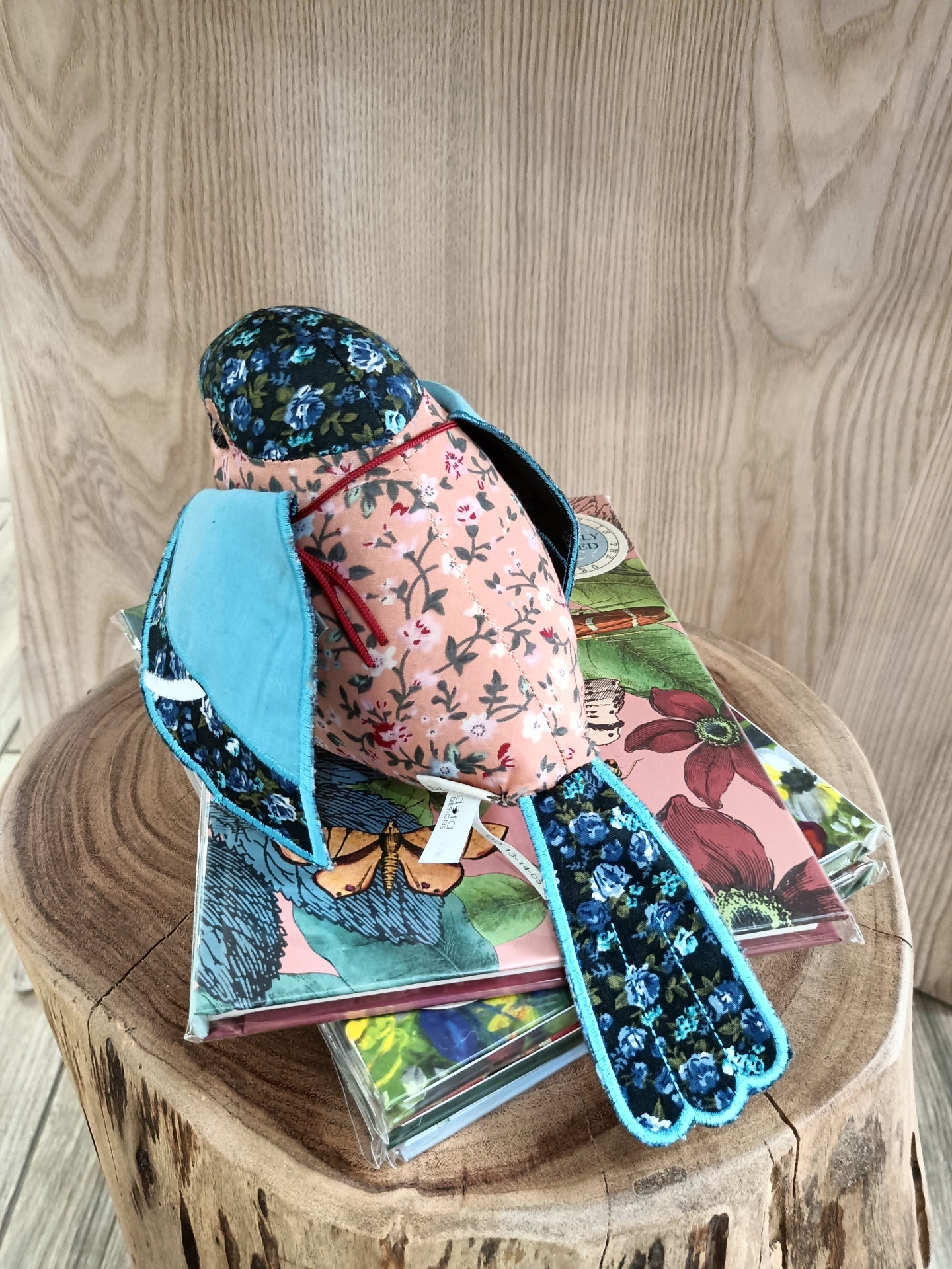Boneco de tecido pássaro floral azul e rosa sobre blocos de notas florais em mesa de madeira
