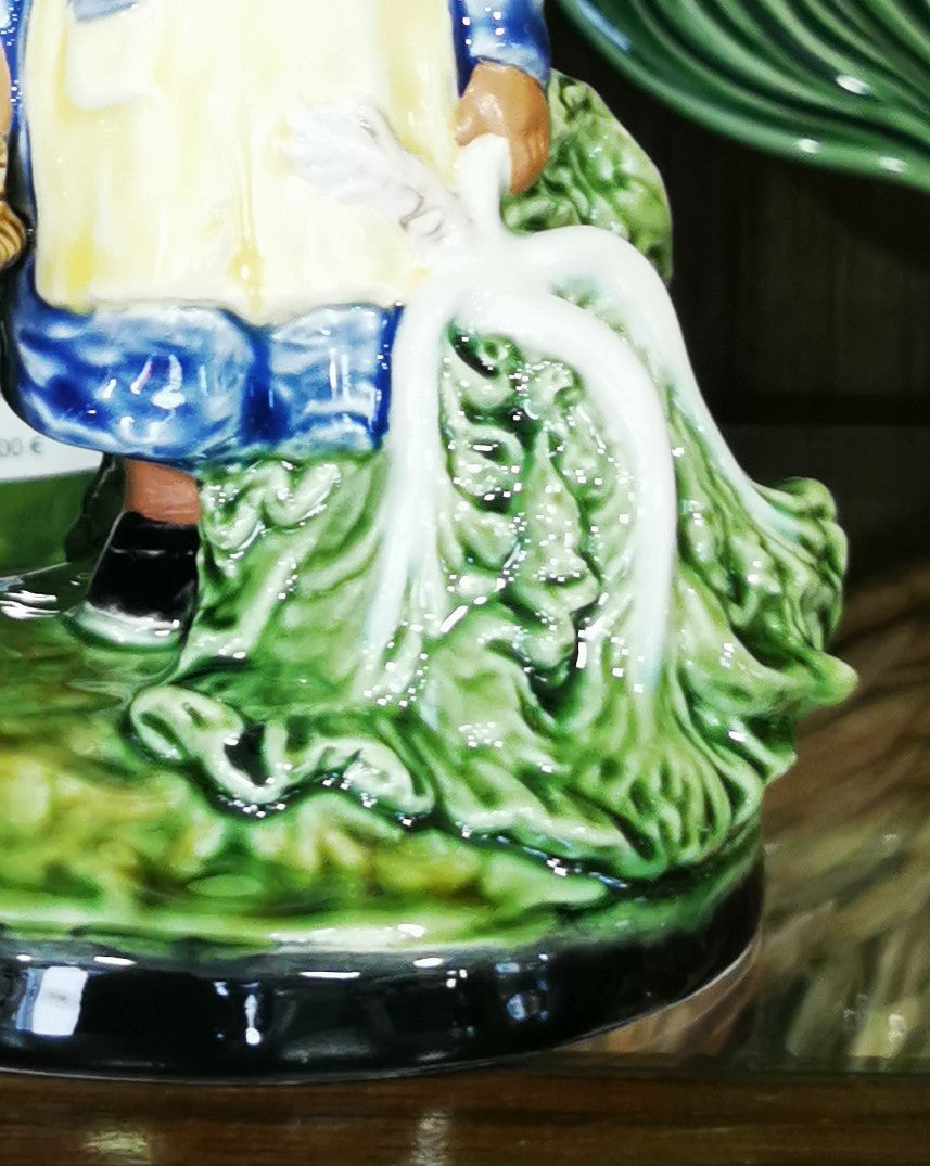 Base cerâmica decorativa com relevo de folhas verdes e parte de figura humana vestida