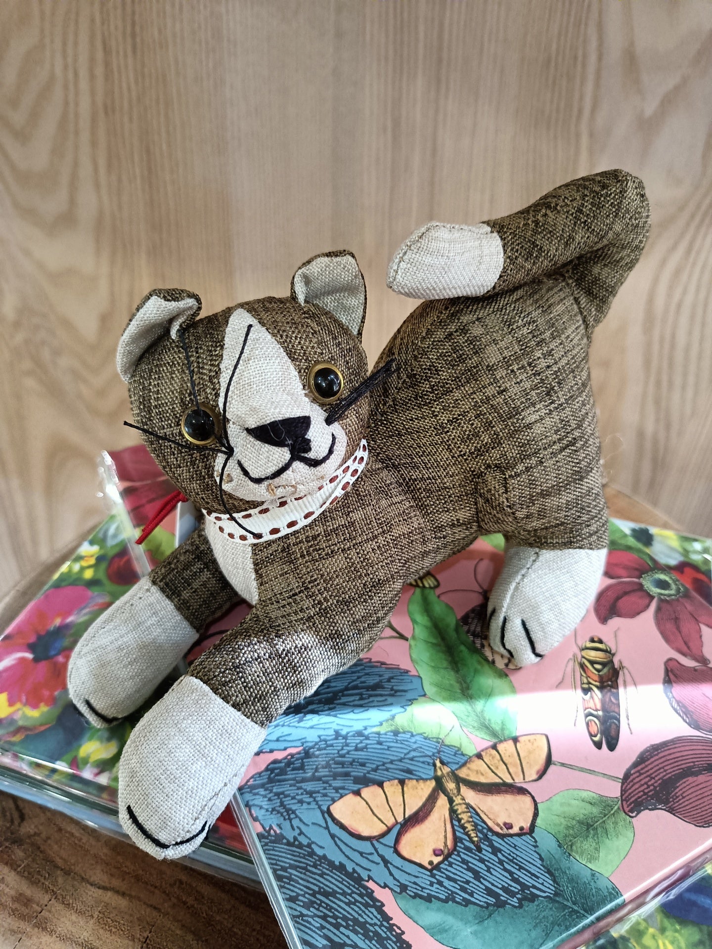 Boneco tecido cão castanho beige olhos plásticos apoiado em caixas metal decoradas flores e borboleta