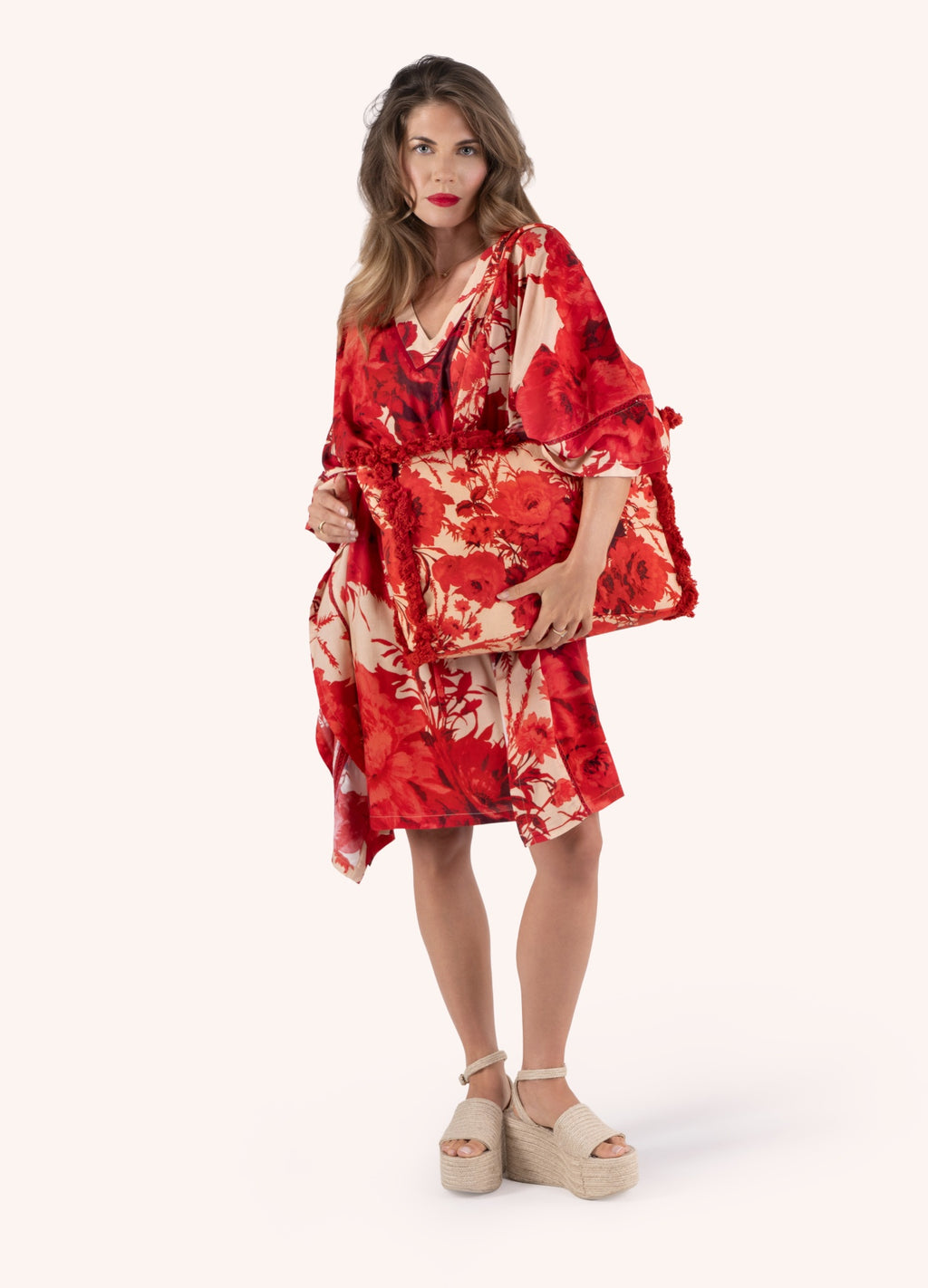Mulher com vestido floral vermelho e bege, mala combinando e sapatos plataforma bege em fundo branco.