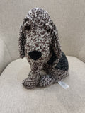 Peluche de cachorro castanho e preto sentado em sofá cinza
