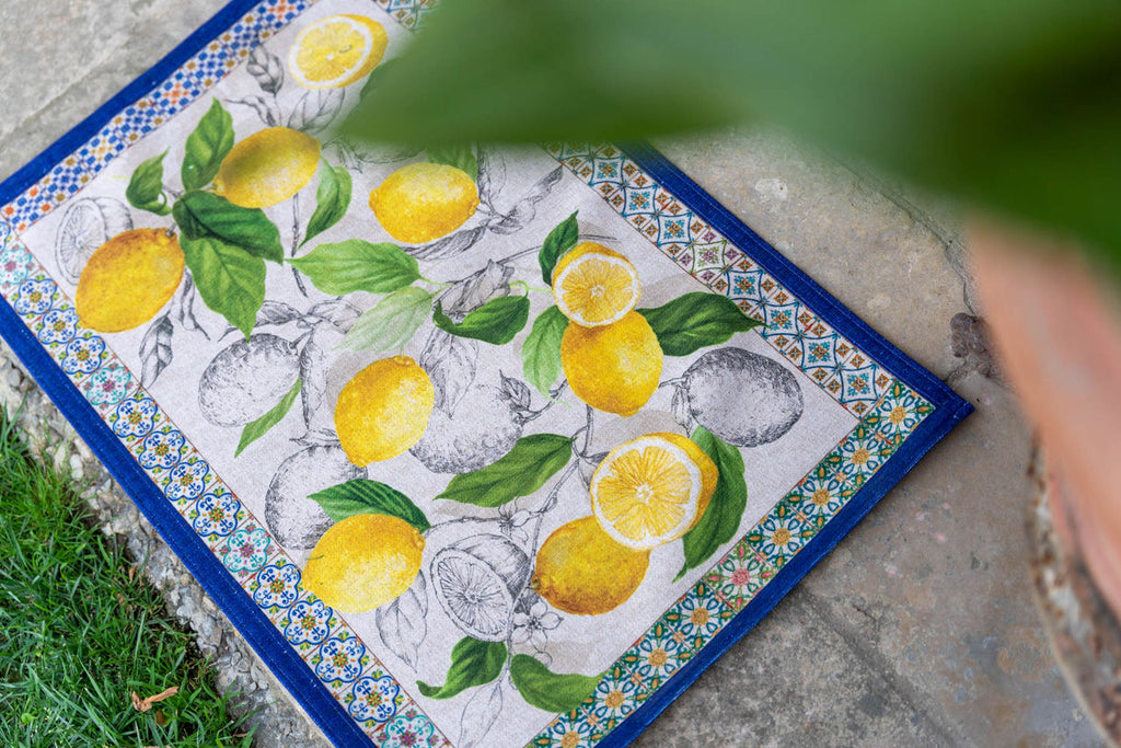 Tapete decorativo retangular com padrão de limões e borda azul sobre chão de pedra ao lado de relva