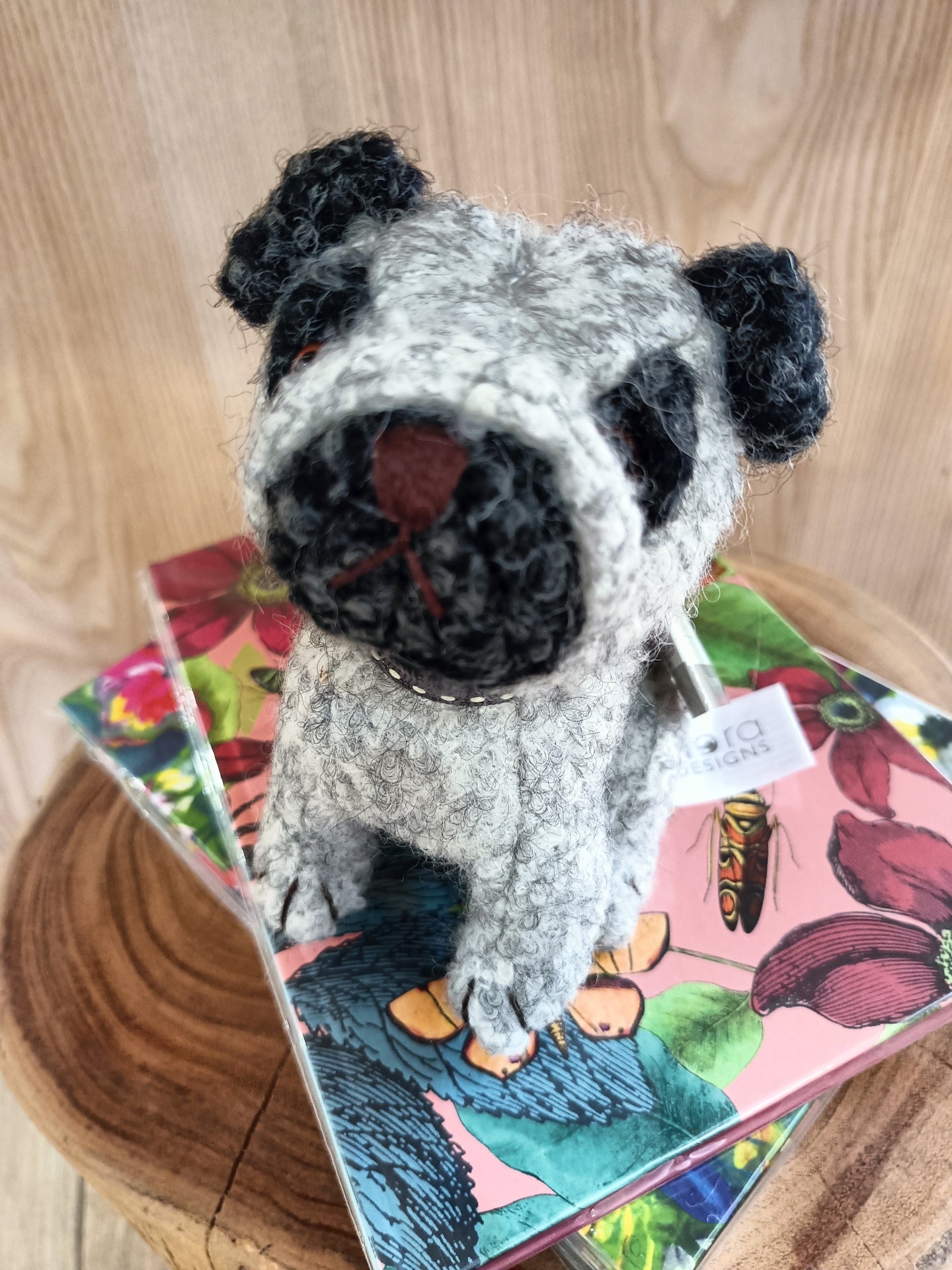 Boneco de cão de lã sentado em cadernos florais sobre base de madeira