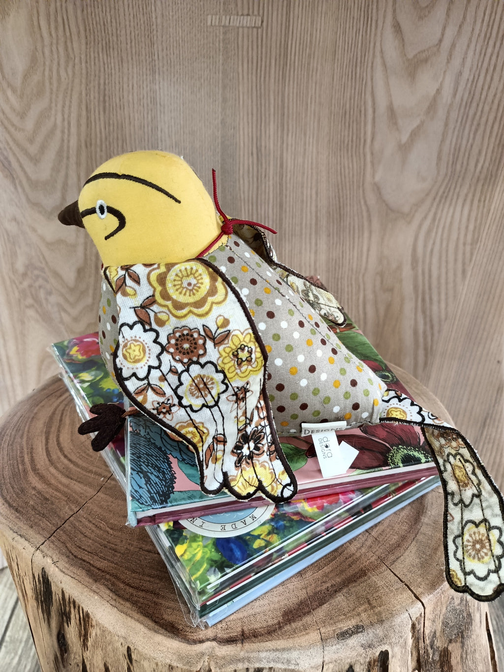 Pássaro de tecido decorativo com padrão floral e bolinhas sobre livros