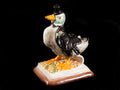 Figuinha de cerâmica pato com vestuário preto e base decorada.