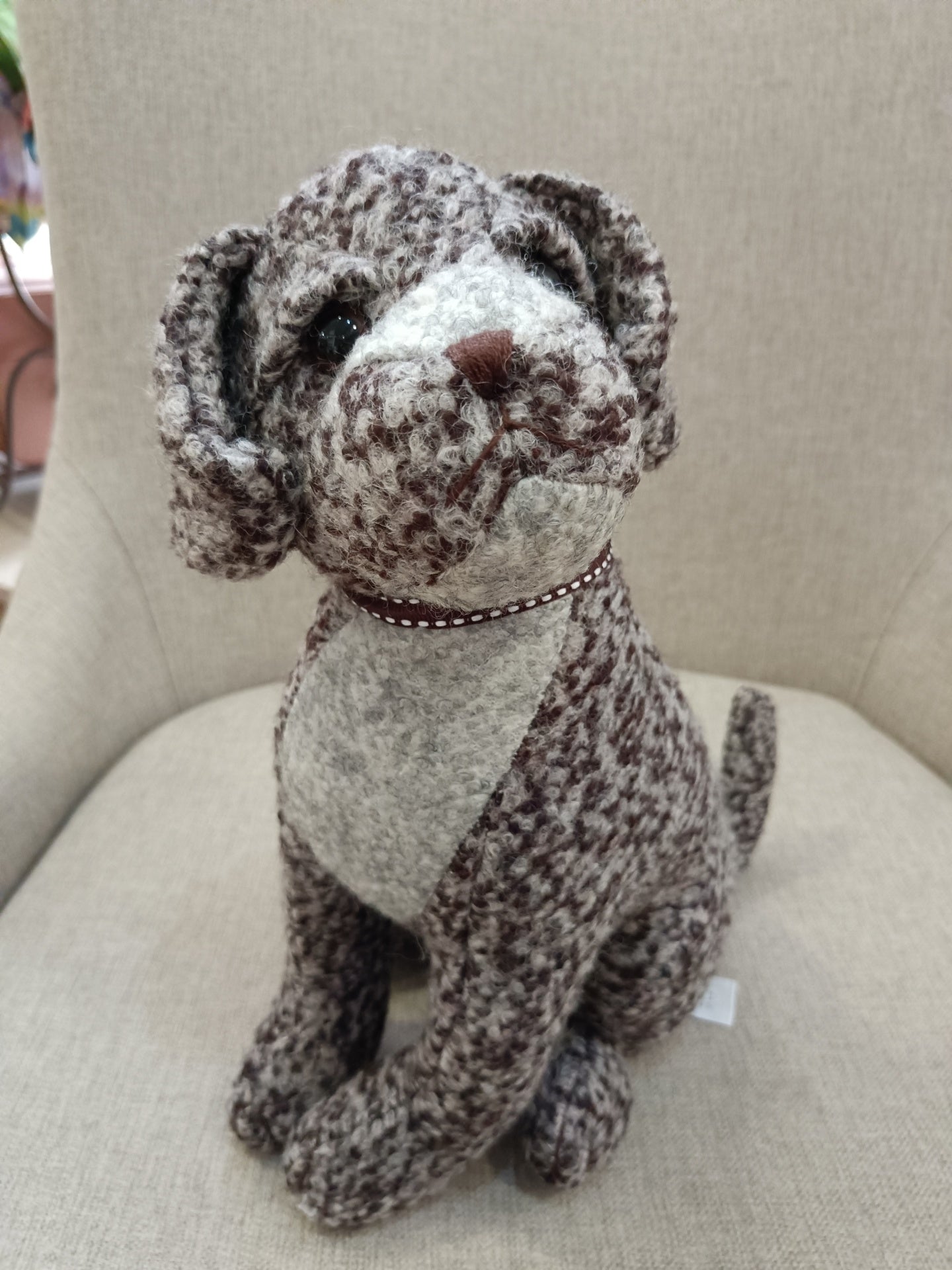 Pelúcia de cão castanha e branca sentada numa cadeira bege