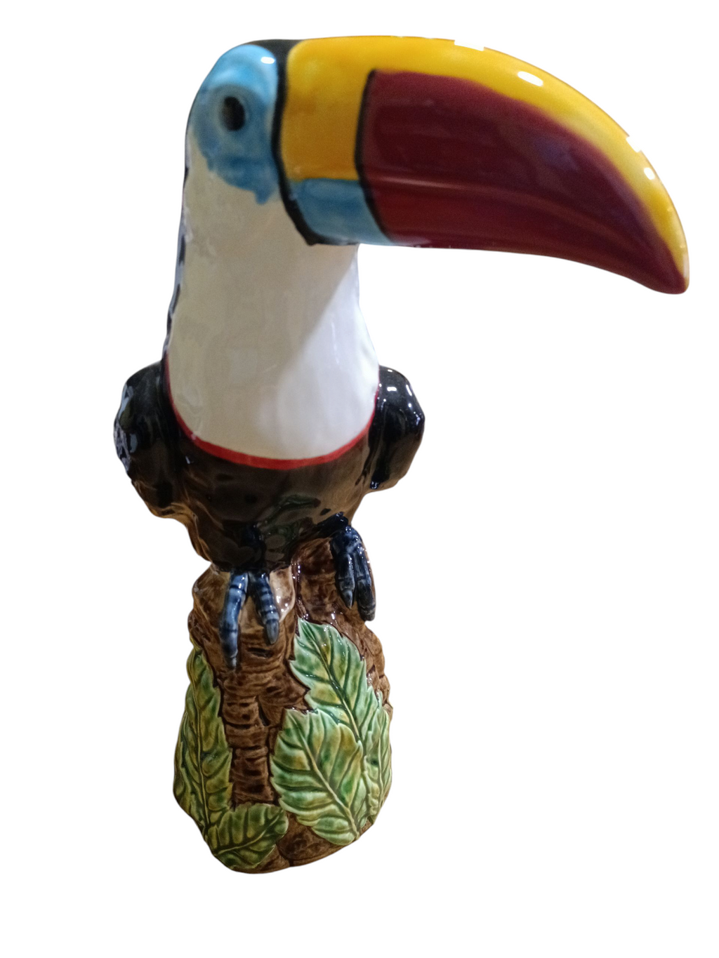 Figura decorativa de tucano colorido em cerâmica com base de folhas verdes.