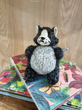 Boneco de peluche gato preto e cinzento em cima de cadernos coloridos com flores e borboletas